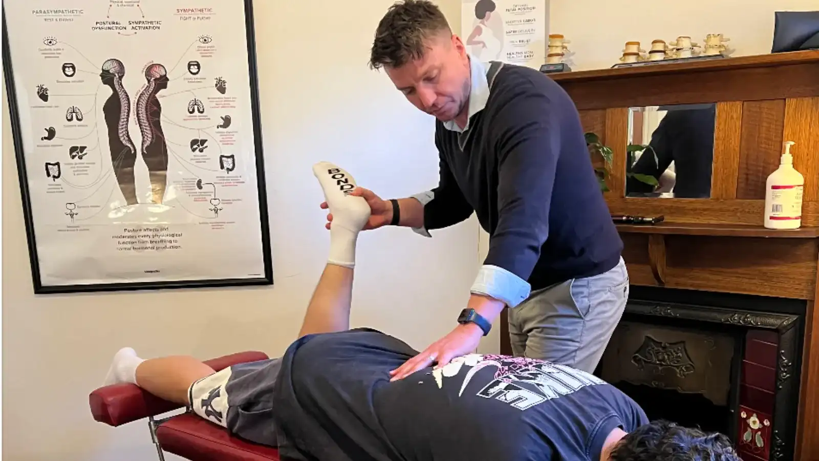 A chiropractor raising a patient's leg during an examination, with a hand on the lower back