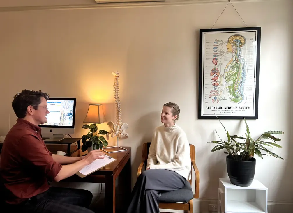 A chiropractor at a desk talking a patient through the findings and the plan