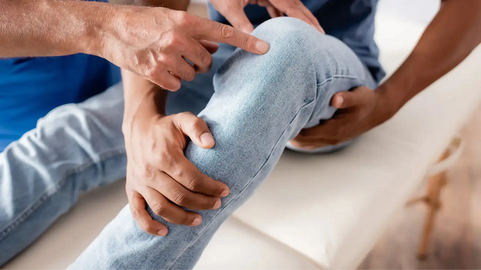 A practitioner examining a seated patient's knee, pointing to the joint line