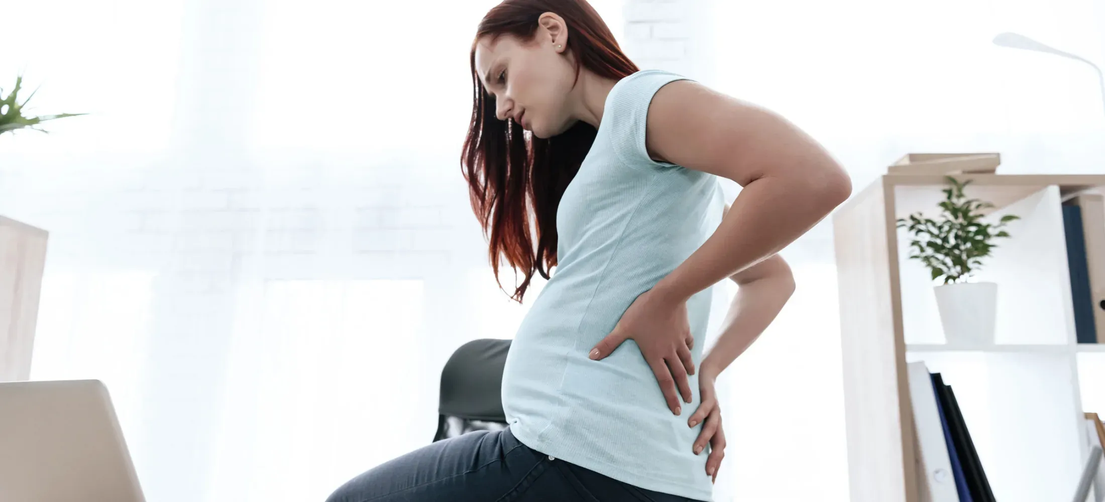 A pregnant woman resting a hand on her lower back and pelvis