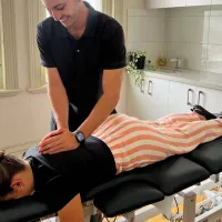 A chiropractor with both hands on the upper back of a woman lying face down on a treatment table