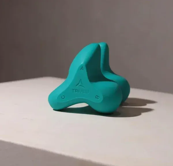 A teal three-lobed silicone device resting on a grey surface