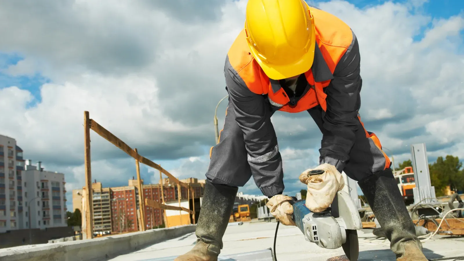 A construction worker bent over a cutting tool on a rooftop site