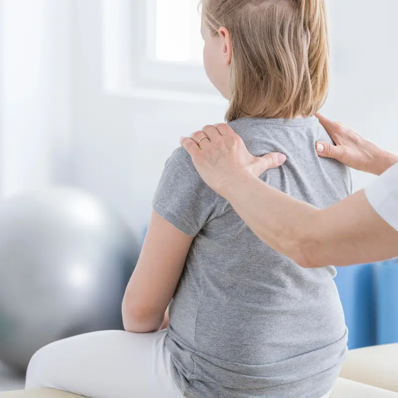 Chiropractor examining a child’s upper back for scoliosis signs